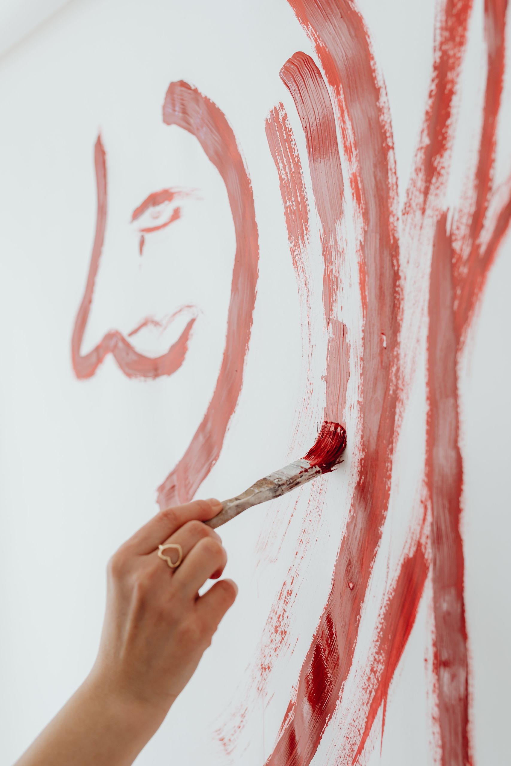 Close-up of a hand painting an abstract red design on a white wall, showing creativity.